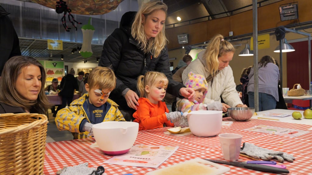 Kinderen en ouders snijden appels tijdens herfstfeest op boerderij.